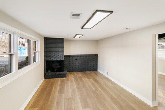 unfurnished living room with light wood finished floors, a fireplace, visible vents, and baseboards