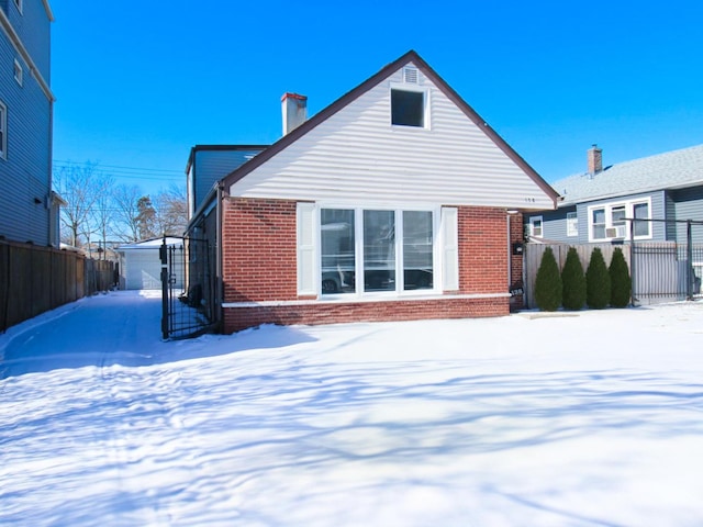 snow covered back of property featuring brick siding, fence, and an outdoor structure