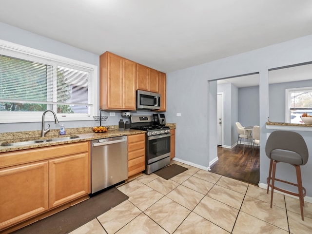 kitchen featuring light tile patterned floors, a sink, baseboards, appliances with stainless steel finishes, and light stone countertops