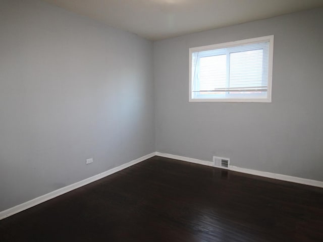 spare room featuring visible vents, baseboards, and dark wood-style flooring