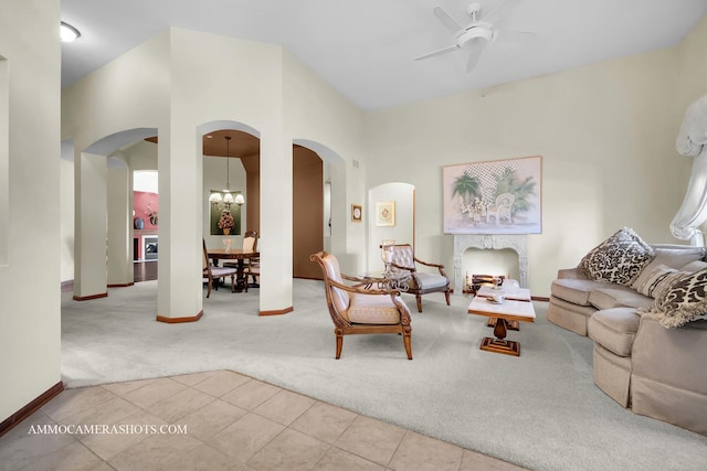 living area featuring arched walkways, carpet flooring, ceiling fan with notable chandelier, and tile patterned floors