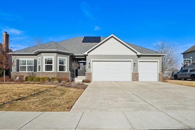 view of front of house featuring brick siding, solar panels, a shingled roof, a garage, and driveway