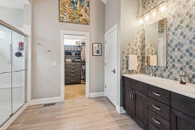 bathroom featuring vanity, baseboards, visible vents, a stall shower, and a walk in closet