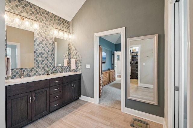 bathroom with lofted ceiling, a sink, wood finished floors, double vanity, and baseboards