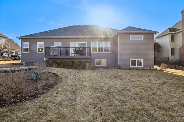 back of property with a lawn, a wooden deck, and fence