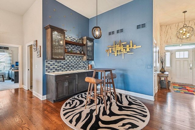 bar featuring visible vents, baseboards, wood finished floors, and a towering ceiling