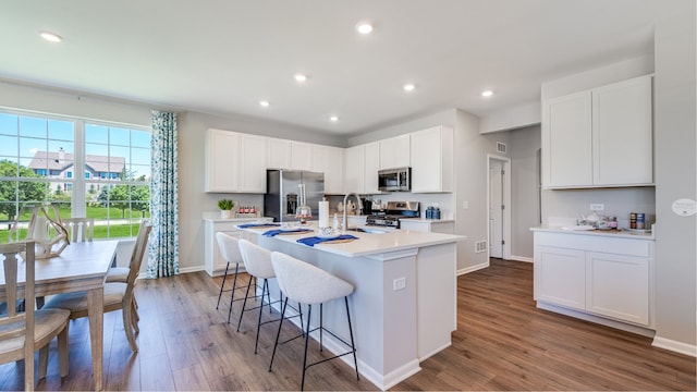 kitchen with stainless steel appliances, wood finished floors, light countertops, an island with sink, and a kitchen bar