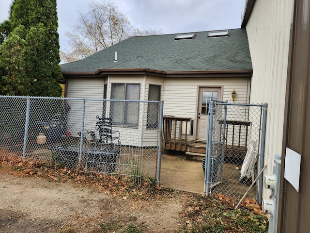 rear view of house with a shingled roof and fence