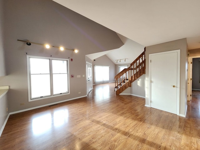 unfurnished living room with baseboards, lofted ceiling, wood finished floors, rail lighting, and stairs