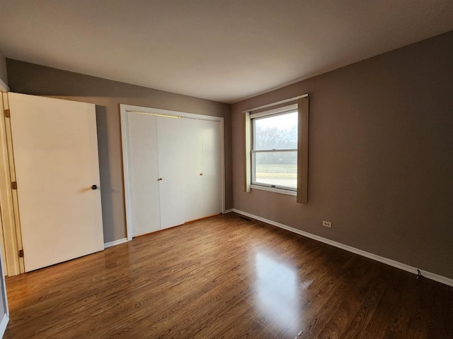 unfurnished bedroom featuring a closet, wood finished floors, and baseboards