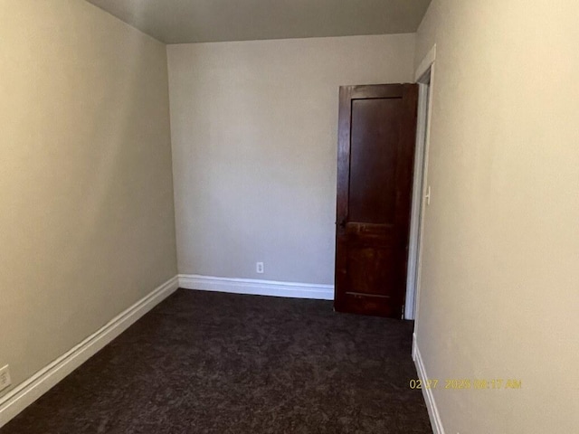 spare room featuring dark colored carpet and baseboards