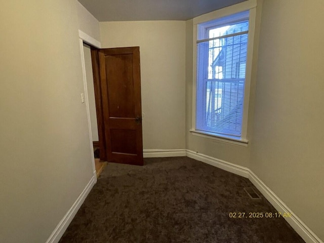 spare room with dark colored carpet, visible vents, and baseboards