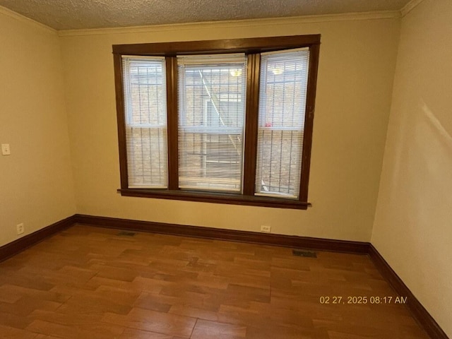 empty room with a textured ceiling, baseboards, wood finished floors, and crown molding