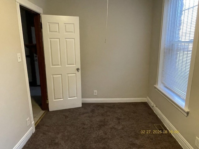 unfurnished room featuring a healthy amount of sunlight, baseboards, and dark colored carpet