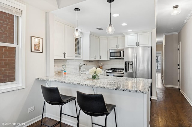 kitchen featuring stainless steel appliances, decorative backsplash, white cabinets, a sink, and a peninsula