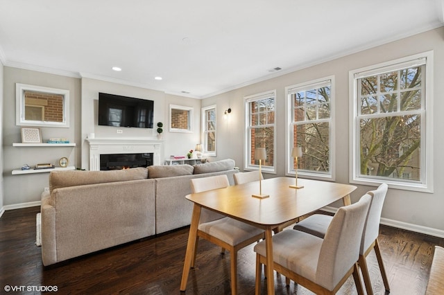 dining space featuring dark wood-style floors, crown molding, visible vents, a lit fireplace, and baseboards