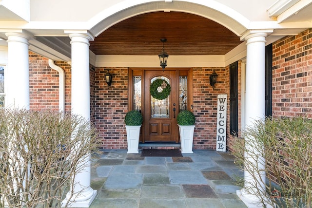 view of exterior entry featuring brick siding and covered porch