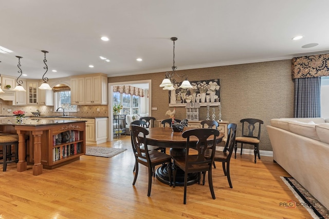 dining space with crown molding, wallpapered walls, light wood-type flooring, and an inviting chandelier