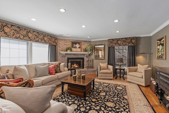 living room featuring wallpapered walls, light wood-style flooring, recessed lighting, ornamental molding, and a brick fireplace