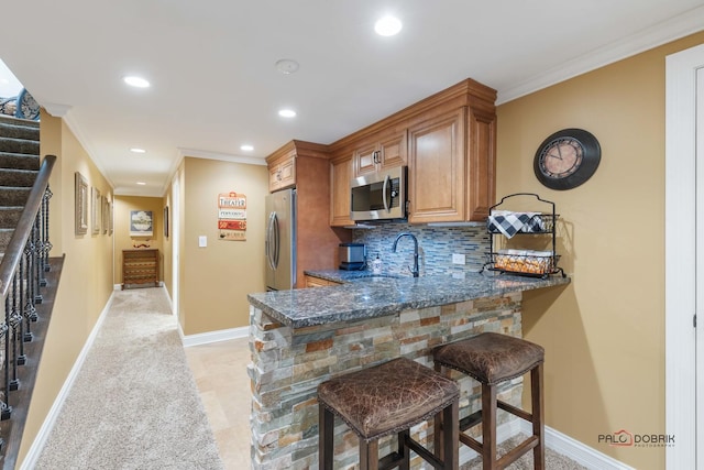 kitchen featuring tasteful backsplash, a breakfast bar, ornamental molding, stainless steel appliances, and a sink