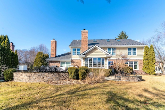 rear view of house with brick siding, fence, a lawn, a chimney, and a patio