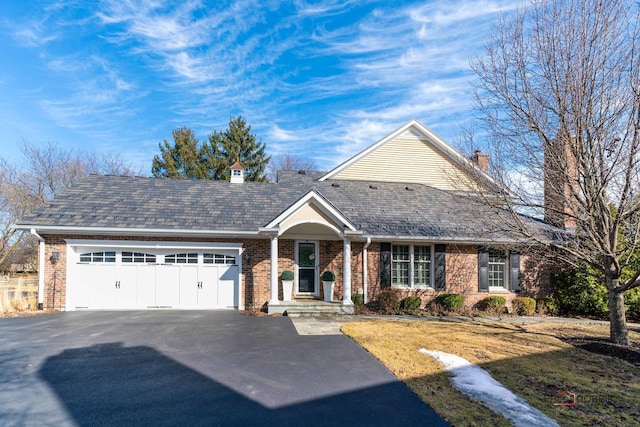 view of front of house with brick siding, driveway, an attached garage, and a chimney