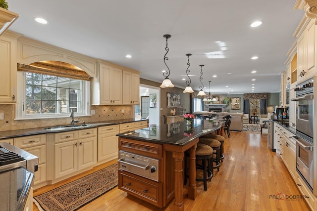 kitchen with a breakfast bar, a sink, a stone fireplace, cream cabinetry, and open floor plan