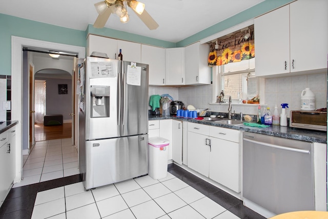 kitchen featuring stainless steel appliances, arched walkways, dark countertops, and decorative backsplash