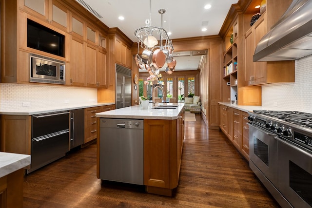 kitchen featuring built in appliances, dark wood-type flooring, a sink, wall chimney exhaust hood, and an inviting chandelier