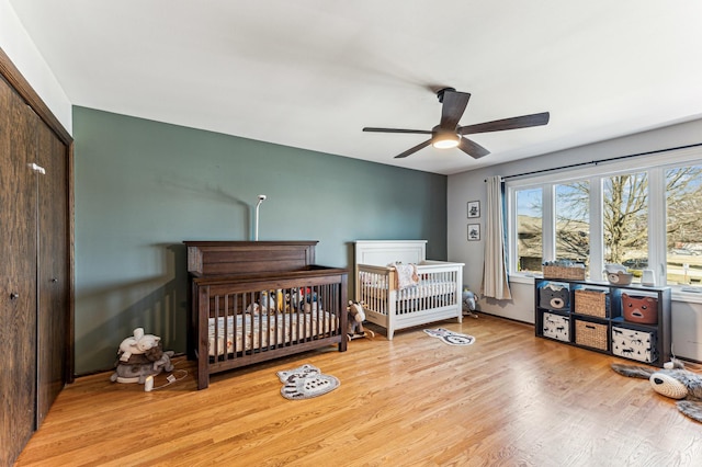 bedroom with a ceiling fan, a nursery area, wood finished floors, and a closet