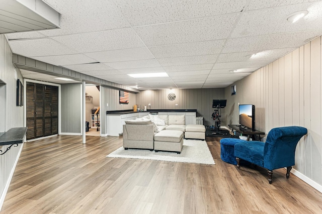 living room featuring baseboards, a paneled ceiling, light wood-style floors, and bar