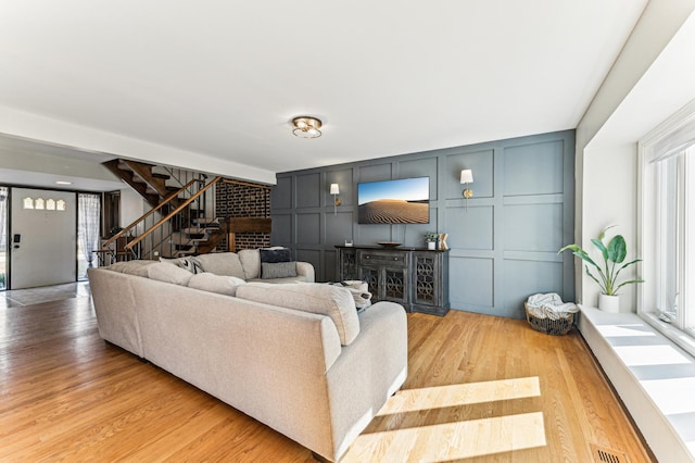 living area featuring stairway, a decorative wall, visible vents, and light wood finished floors