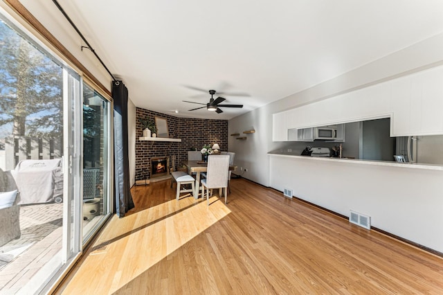 interior space with light wood-style flooring, visible vents, brick wall, and ceiling fan