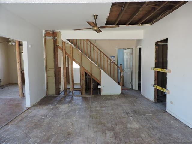 unfurnished living room featuring ceiling fan and stairway