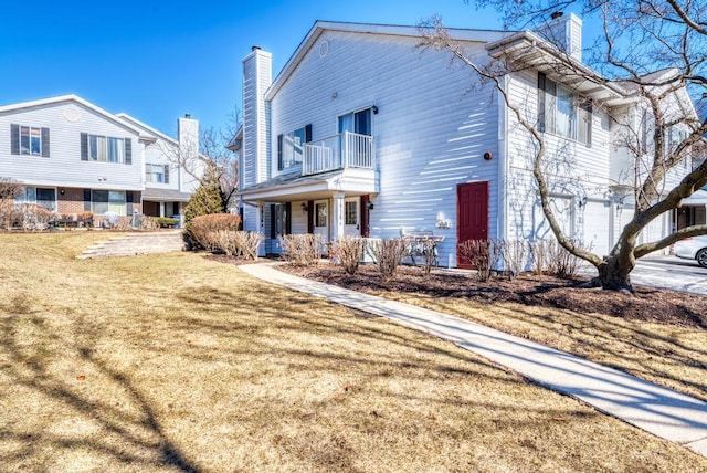 exterior space featuring a yard, a chimney, an attached garage, a balcony, and driveway