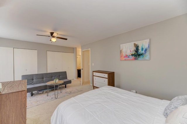 bedroom with a ceiling fan, two closets, and light colored carpet