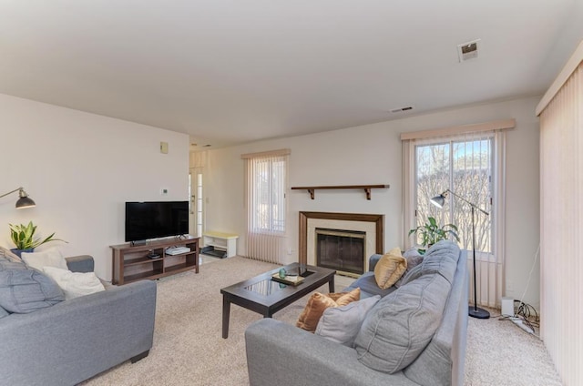 living area featuring light carpet, a glass covered fireplace, and visible vents