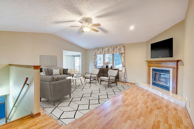 living room with a ceiling fan, light wood-style flooring, vaulted ceiling, a textured ceiling, and a high end fireplace