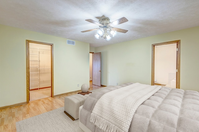 bedroom with visible vents, a spacious closet, light wood-style floors, a textured ceiling, and baseboards