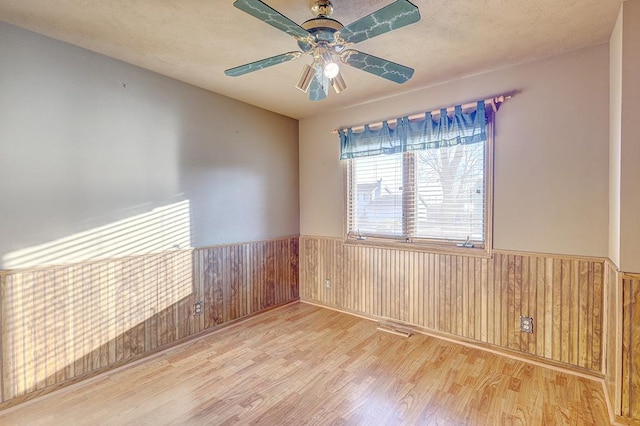 empty room with a wainscoted wall, visible vents, wood walls, a textured ceiling, and wood finished floors