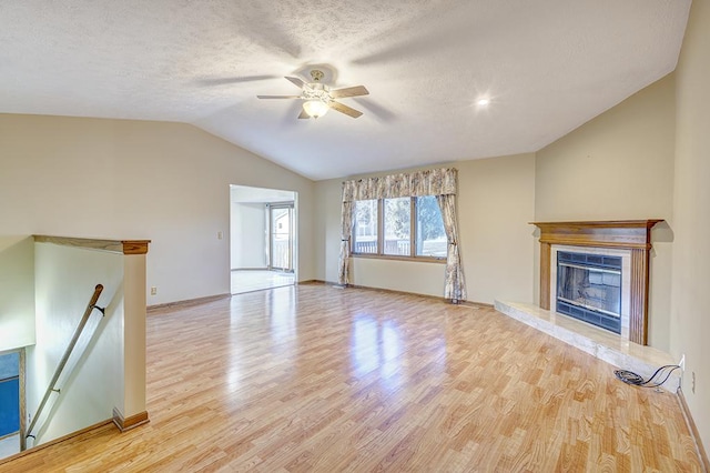 unfurnished living room featuring a fireplace with raised hearth, a textured ceiling, ceiling fan, vaulted ceiling, and light wood finished floors