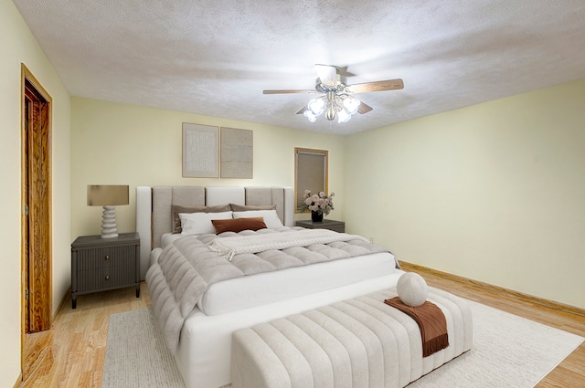 bedroom with a textured ceiling, light wood finished floors, a ceiling fan, and baseboards