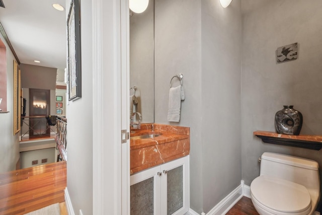 half bath with baseboards, vanity, and toilet