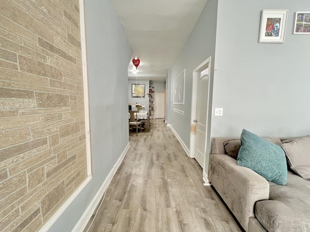 hallway with brick wall, light wood finished floors, an accent wall, and baseboards