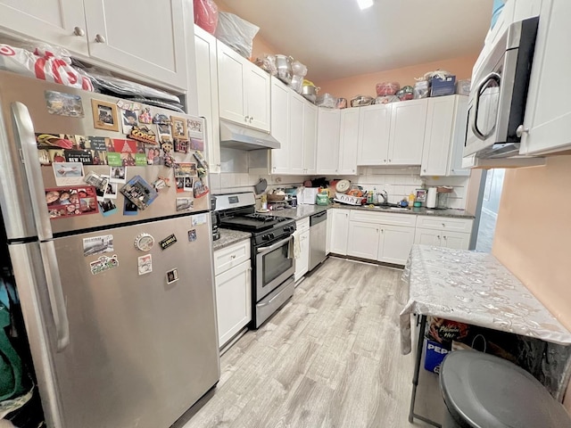 kitchen featuring light wood finished floors, white cabinets, appliances with stainless steel finishes, under cabinet range hood, and backsplash