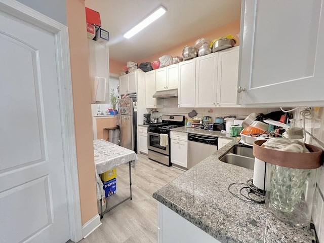 kitchen featuring under cabinet range hood, stainless steel appliances, white cabinetry, light wood-style floors, and tasteful backsplash