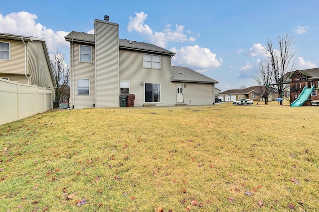 rear view of house featuring a chimney, a lawn, a playground, and fence