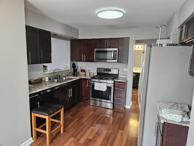 kitchen with light stone counters, dark wood-style floors, appliances with stainless steel finishes, a sink, and dark brown cabinets