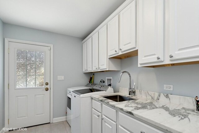 clothes washing area featuring light tile patterned floors, cabinet space, washing machine and dryer, a sink, and baseboards