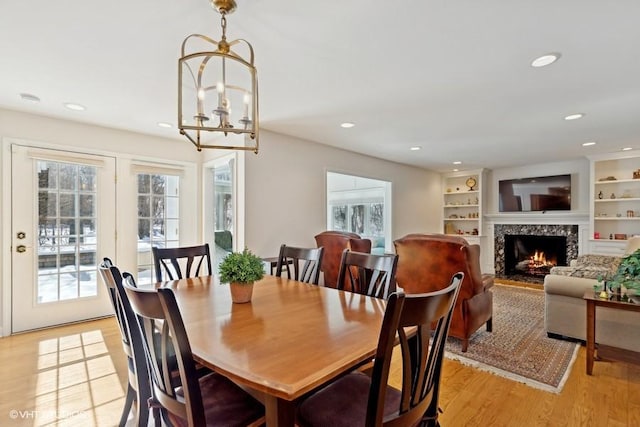 dining room with a chandelier, a premium fireplace, light wood-style flooring, and recessed lighting